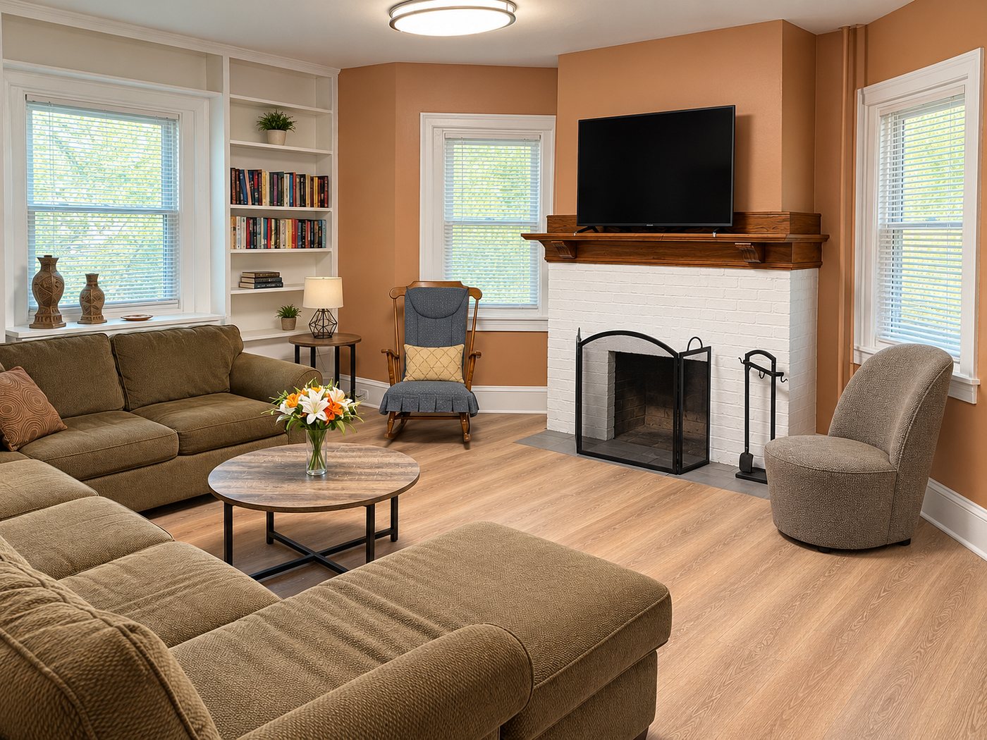 Common room in an Evo Living home: a sofa and armchairs around a white brick fireplace, a wall of books.